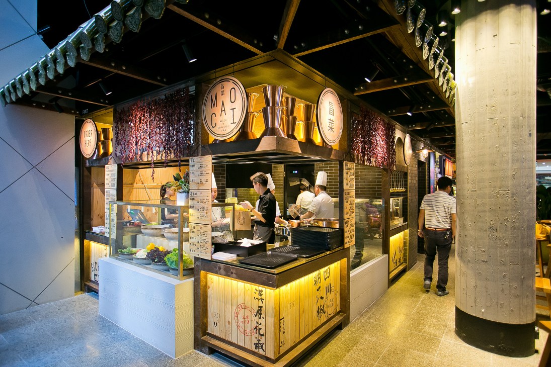An Asian noodle shop with illuminated signage in a modern shopping mall food court.
