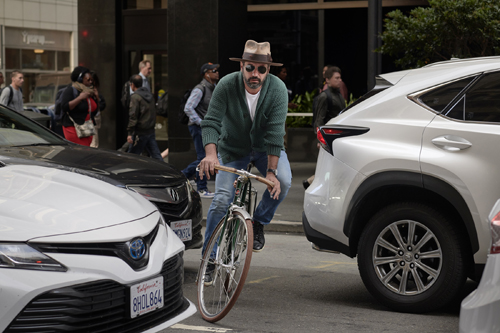 Man in cycling gear riding a bicycle between parked cars on an urban street.