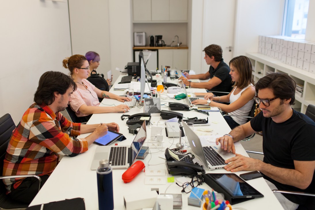 Wieden + Kennedy São Paulo creative team in casual meeting around a long desk with laptops and notebooks.