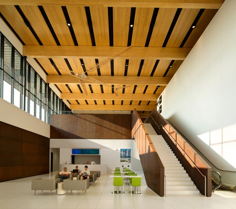 Modern airport terminal interior with wooden beam ceiling, white walls, and central atrium with seating areas.