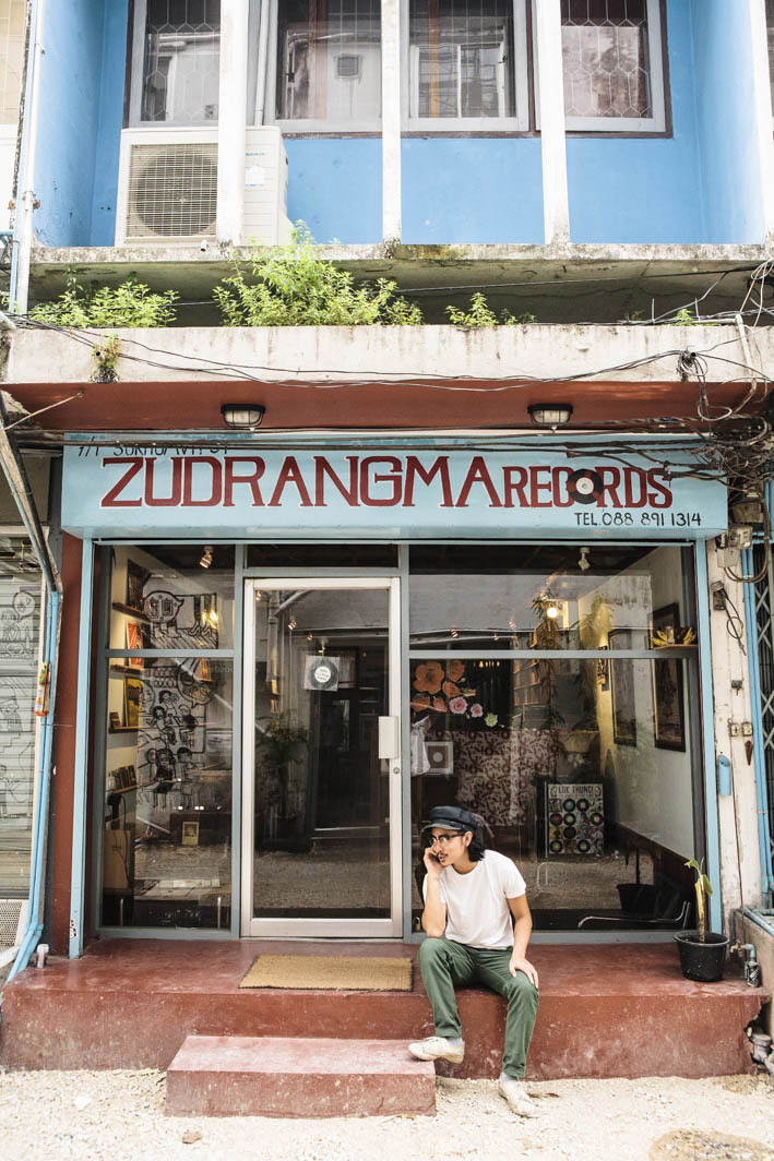 Person sitting outside ZudRangMa Records storefront in Bangkok with blue signage and vinyl records visible inside