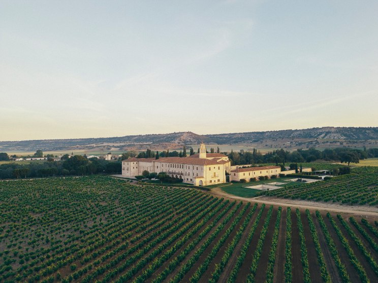 Aerial view of historic Abadía Retuerta monastery surrounded by neat rows of vineyard plantings in Spanish countryside