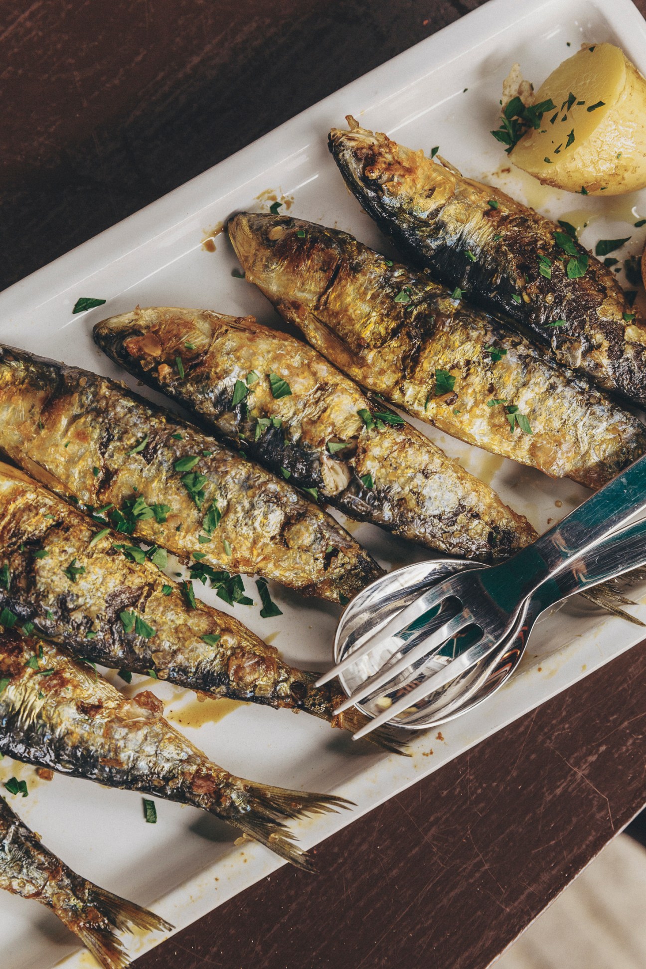 Grilled whole sardines garnished with herbs served on white parchment paper with lemon and fork