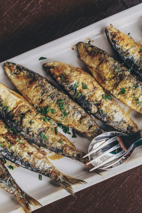 Grilled sardines arranged on white parchment paper with serving utensils