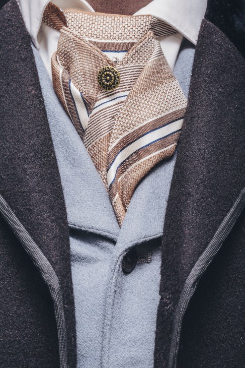 Close-up detail of an ornate brown and cream striped morning coat with decorative pin being crafted for The Gilded Age
