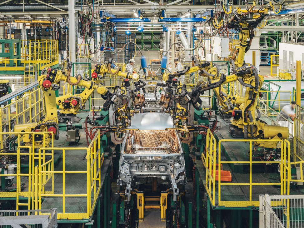Yellow robotic arms welding car bodies on an automotive assembly line in a modern factory