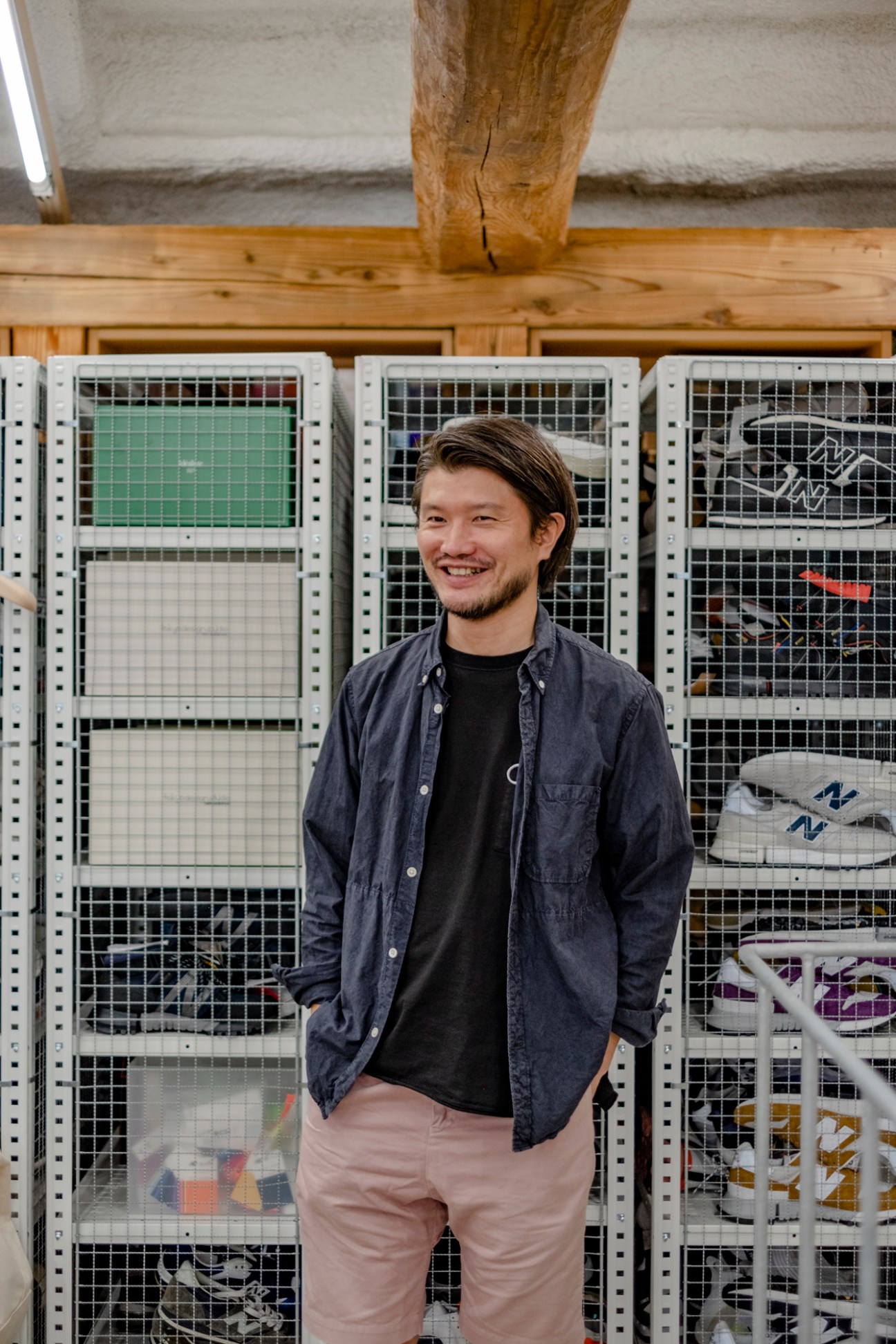 Man smiling in workshop with wooden beams and metal storage shelving containing materials