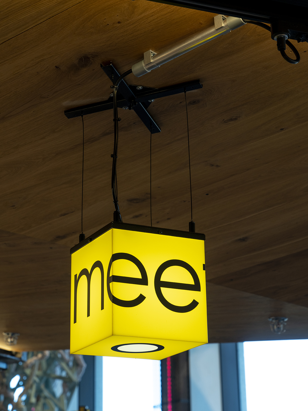 Yellow cube-shaped pendant light with black text hanging from wooden ceiling