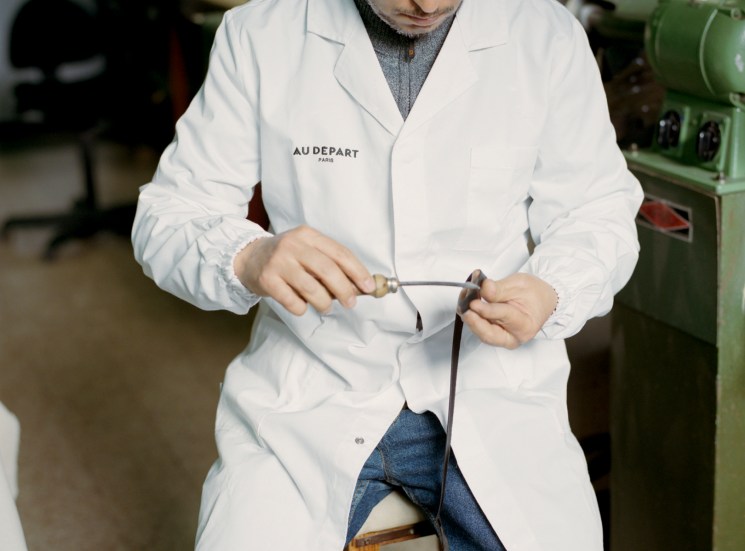 Artisan in white lab coat working on detailed craftswork at Au Départ's Milan workshop