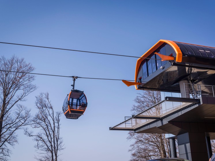 Modern cable car station with orange accents and glass facade against clear blue sky