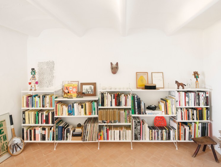A low white modular bookshelf filled with books and small decorative objects against a white wall.
