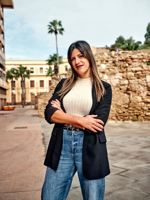 Tour guide Jennifer Aragón standing with arms crossed, smiling at camera in outdoor Mediterranean setting