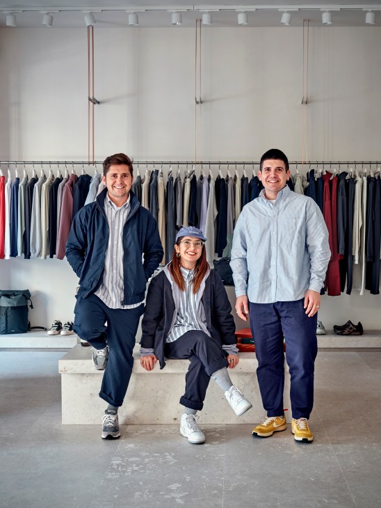 Three people pose in modern clothing showroom with hanging garments and minimalist design
