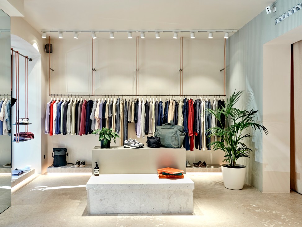 Modern minimalist clothing store interior with concrete fixtures, hanging garments, and potted plants