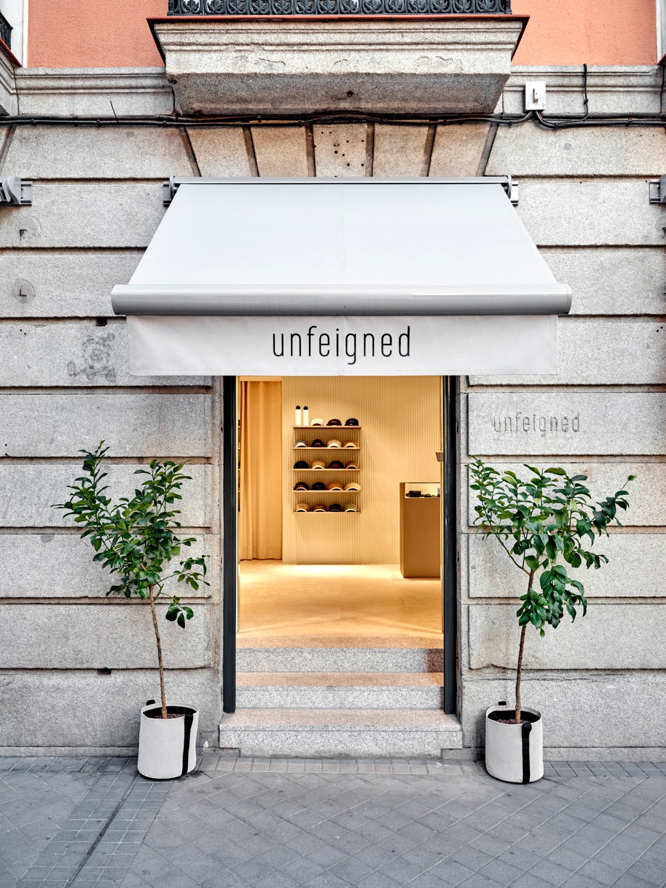Unfeigned boutique storefront in Madrid with white awning, minimalist design, and warm wooden interior visible through entrance.