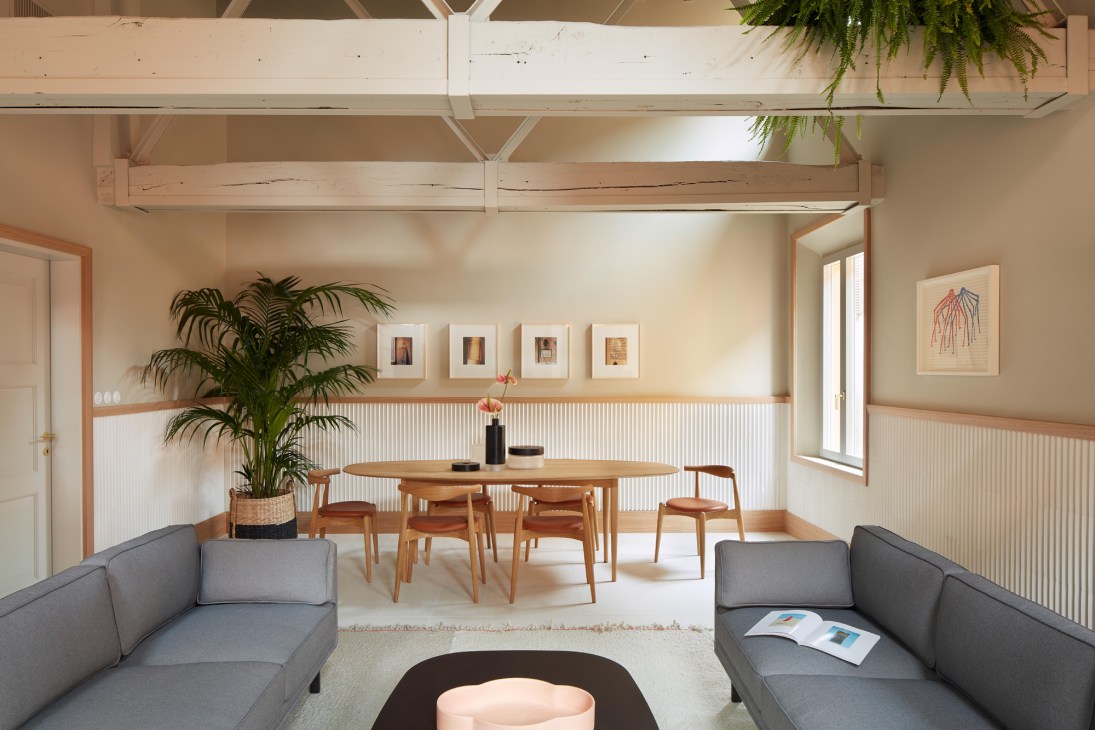 Modern minimalist interior with wooden dining table, gray sofas, white walls, and exposed beam ceiling in Casa Mutina guesthouse.