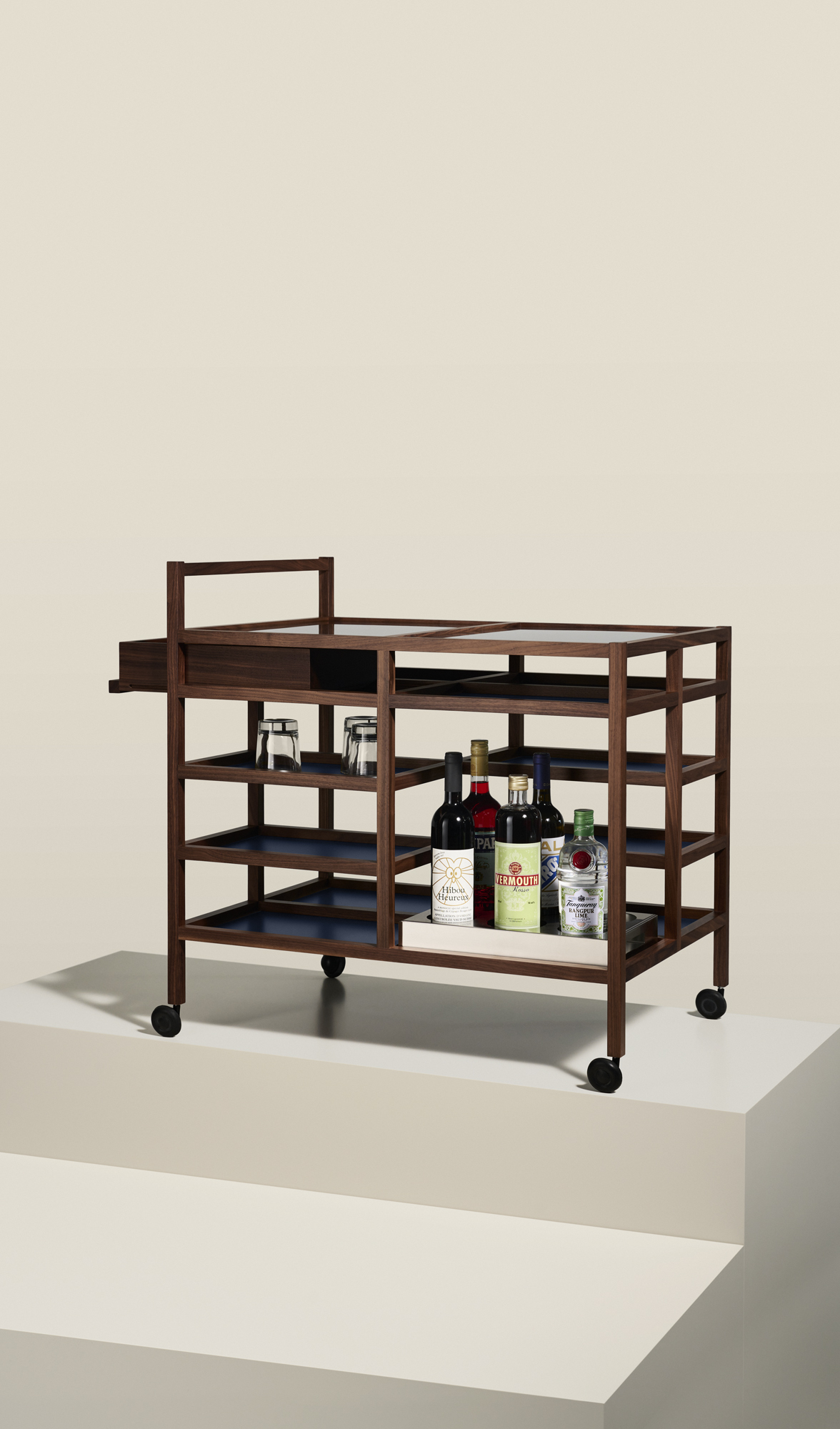 Bodil Kjaer 657 Serving Cart by Cassina featuring walnut wood frame with multiple shelves and bottles displayed on wheels