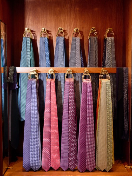 Elegant neckties in various patterns and colors displayed on brass rings mounted on wooden rack in menswear store
