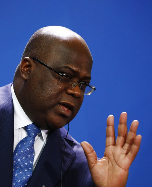 African man in blue suit and glasses speaking with raised hand