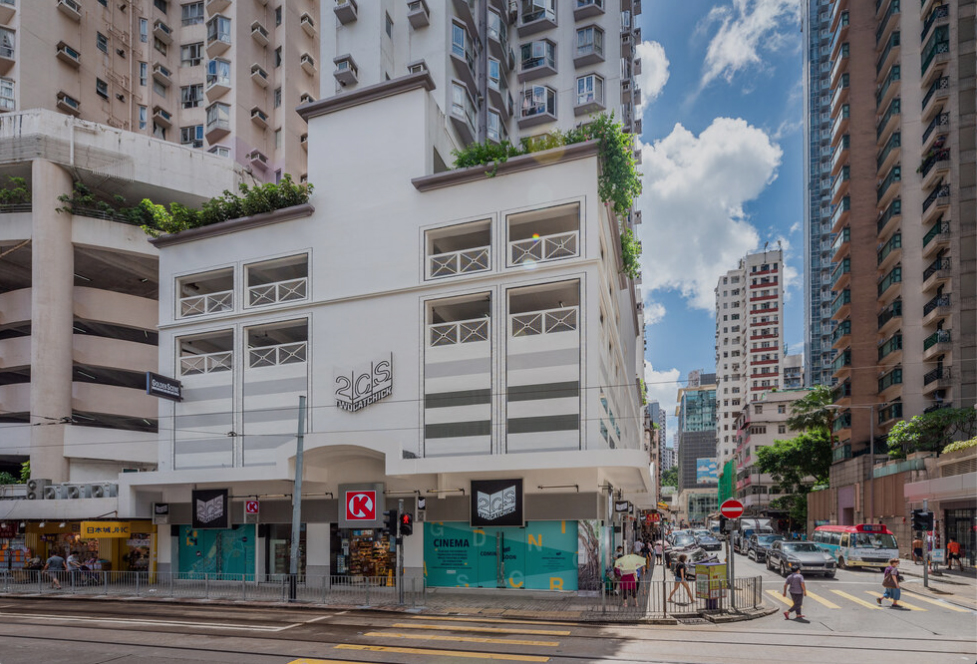 Modern white cinema building with glass windows and green signage on urban street with high-rise apartments