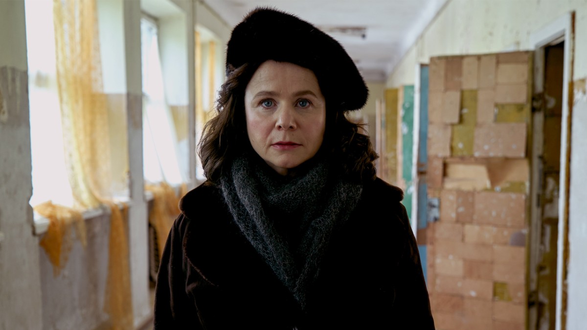 Emily Watson as a Soviet physicist in the Chernobyl mini-series, wearing a black coat and hat in a institutional hallway.