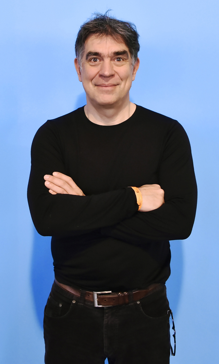 Man in black sweater and jeans with arms crossed standing against blue background