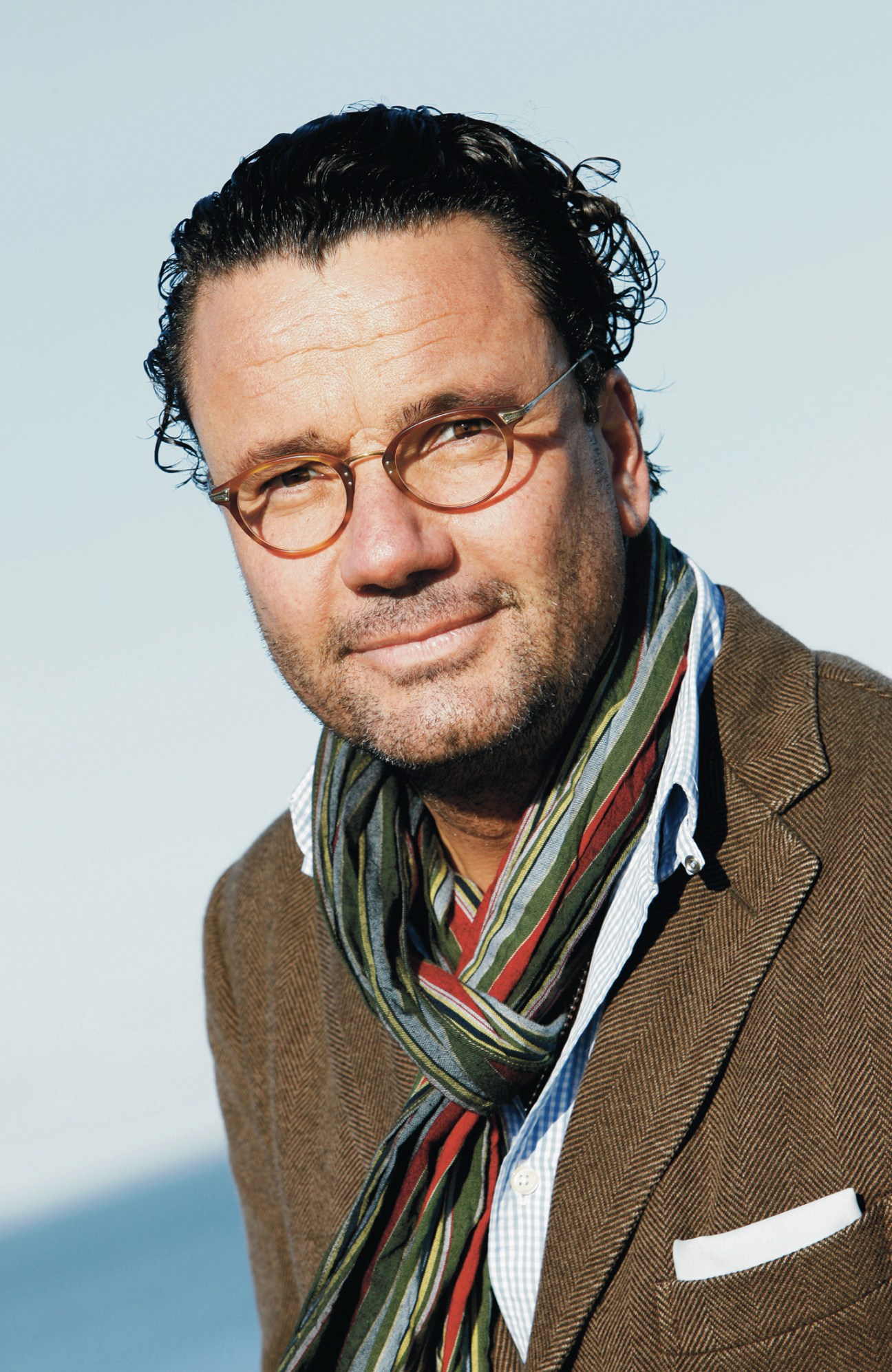 Man in brown blazer and colorful striped scarf wearing glasses