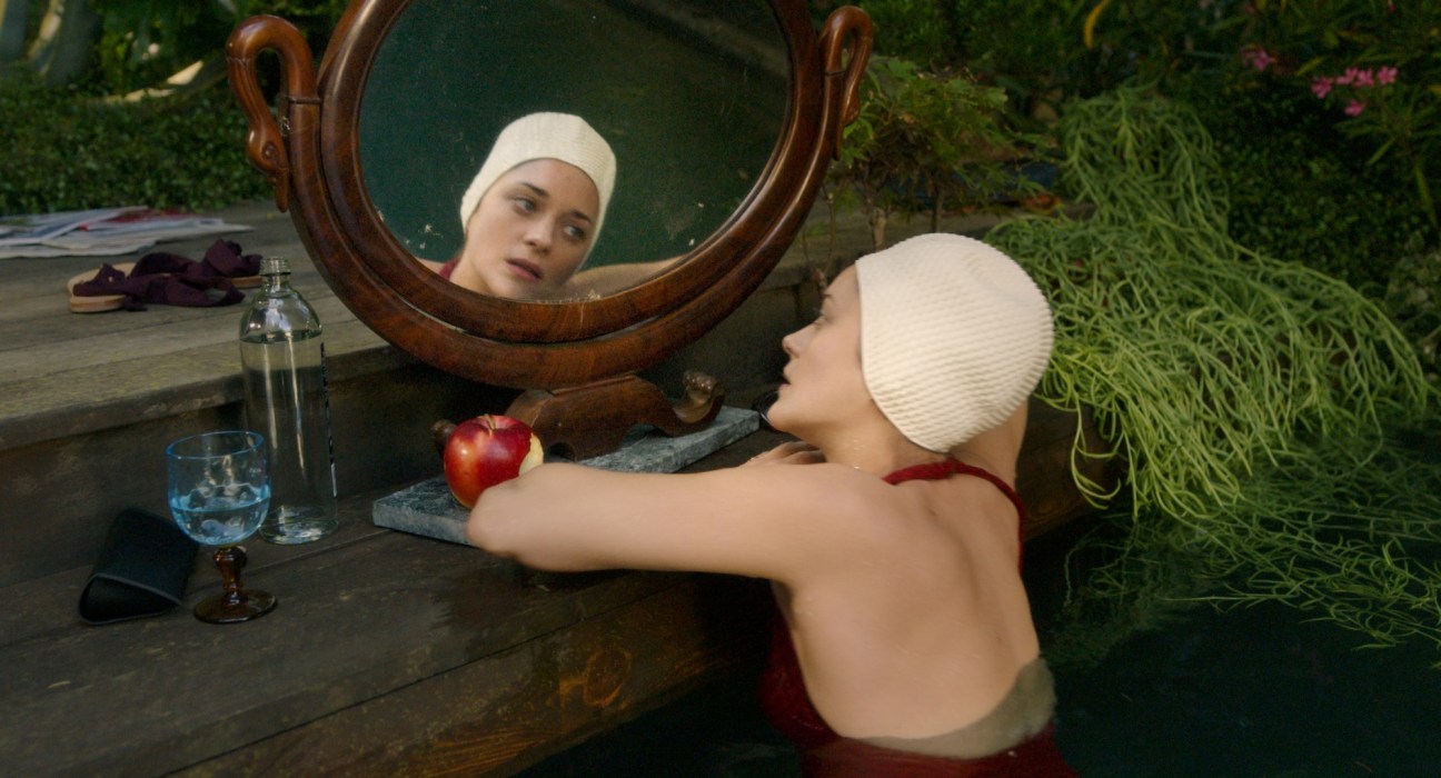 Woman in cream swimming cap looking in ornate mirror while in water, holding red apple