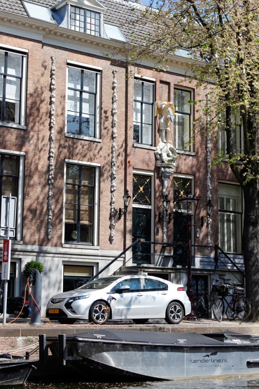 White electric car charging at a station on an Amsterdam street with traditional brick canal houses