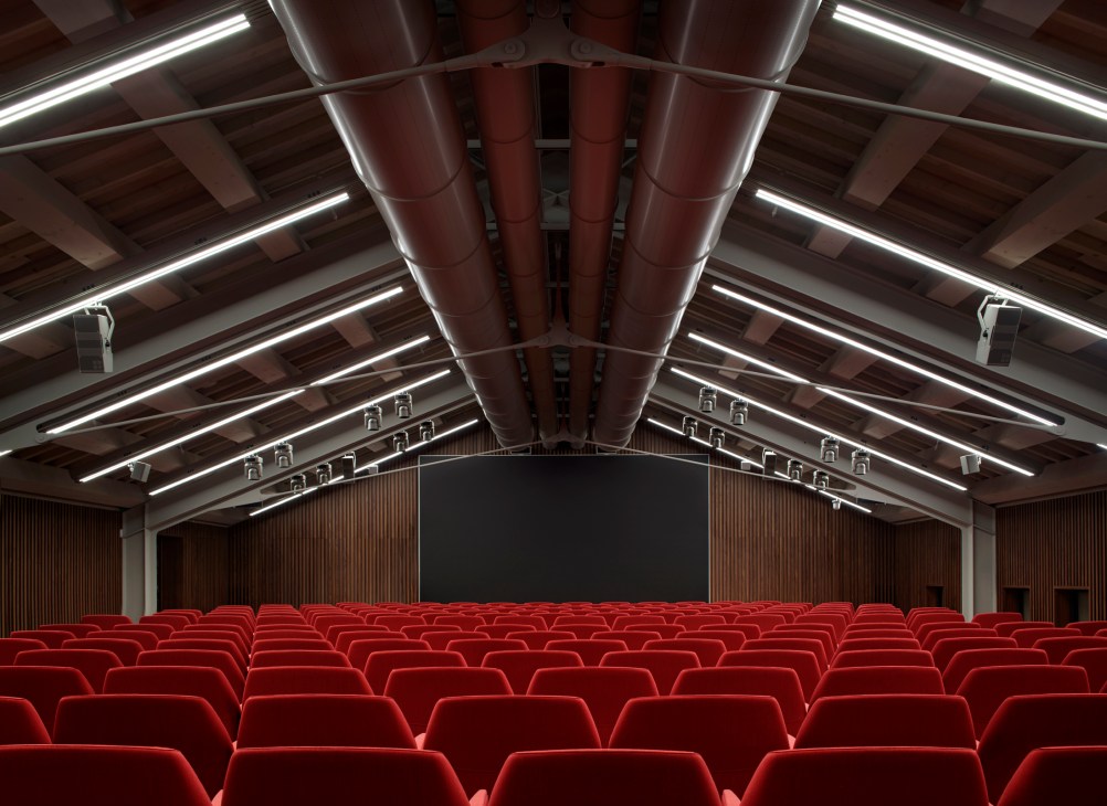 Modern auditorium with red velvet seating and exposed ceiling beams in renovated Procuratie Vecchie building