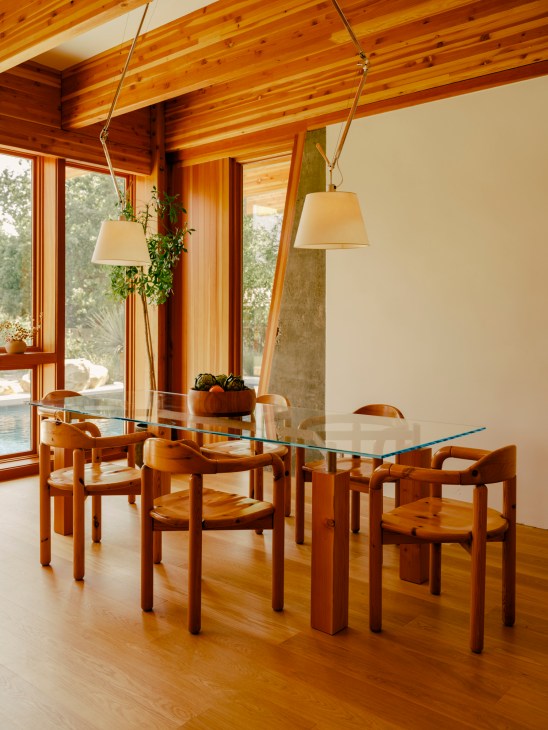 Dining room with glass-topped table surrounded by wooden chairs under pendant lights with exposed ceiling beams
