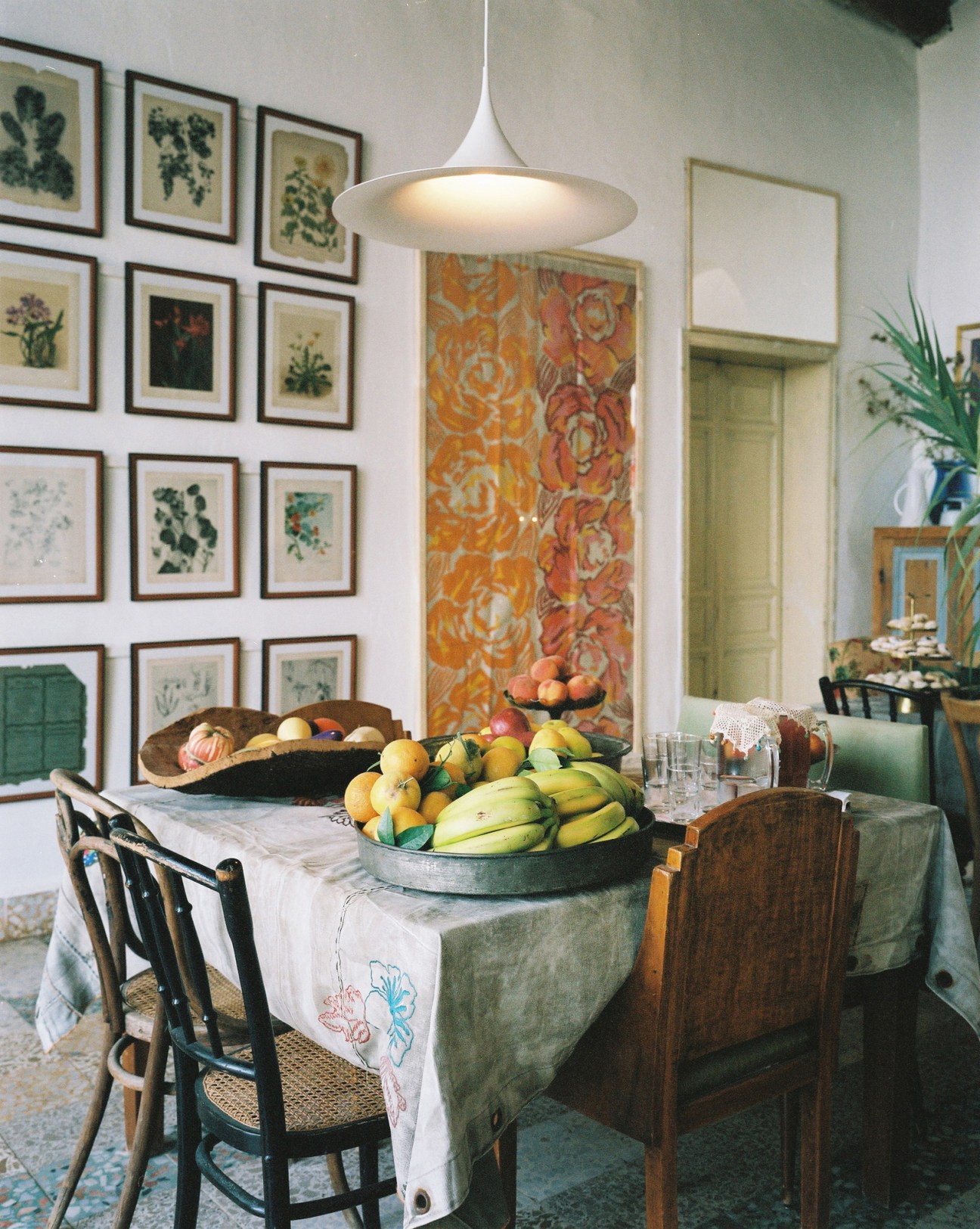 Dining room with pendant light, gallery wall of framed botanical prints, and table with fresh fruit