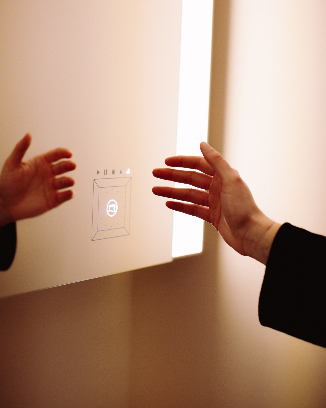 Hands gesturing toward an illuminated touch-free light switch panel on a wall.