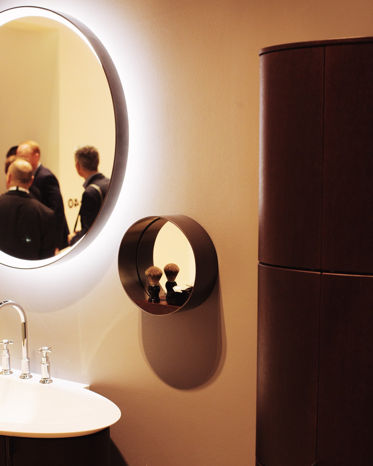 Modern bathroom with illuminated circular mirrors reflecting people, white sink, and dark wooden cabinet.