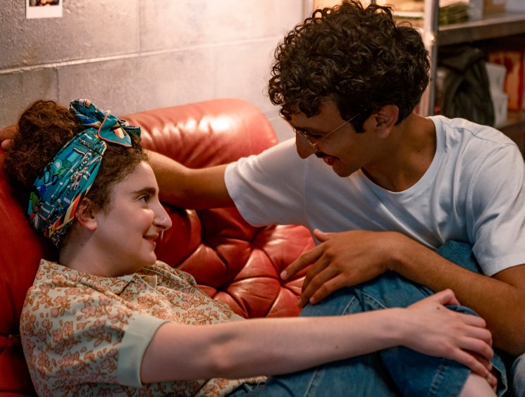 Two people sitting close together on a red leather couch in an intimate scene from Standing Up