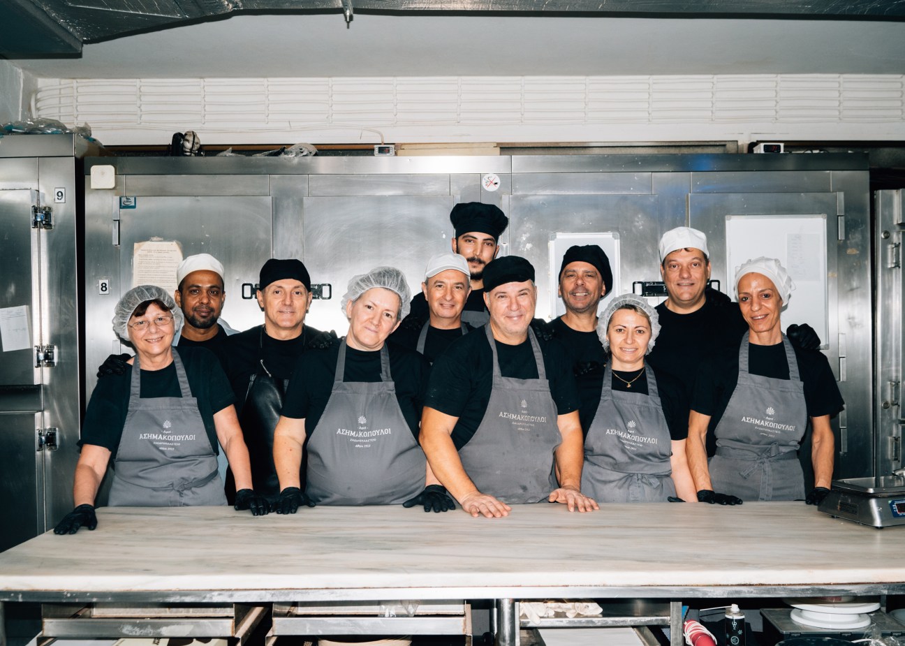 Team of bakers in matching gray aprons and chef hats posing together in modern commercial kitchen