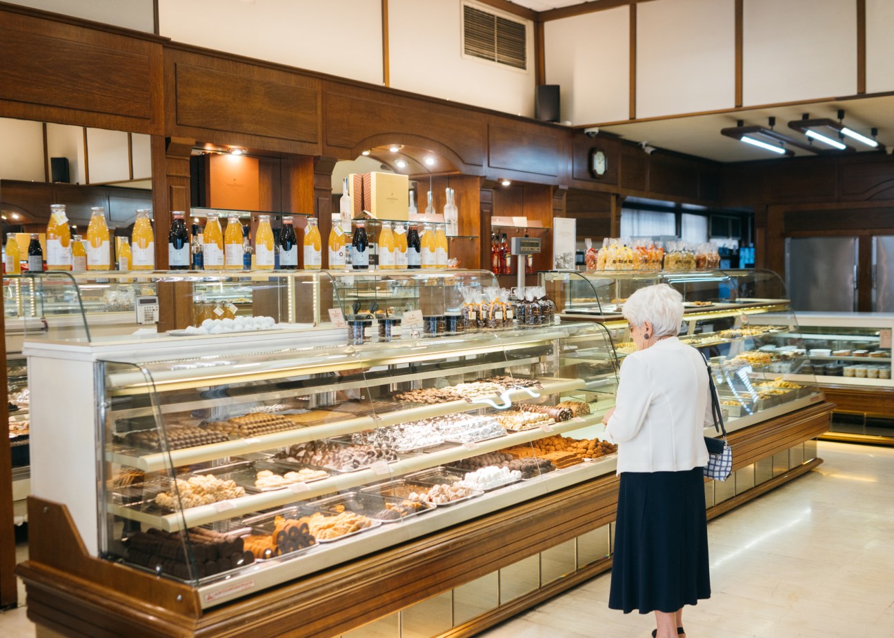 Elderly woman browsing glass display cases filled with traditional Lebkuchen and baked goods in upscale German bakery