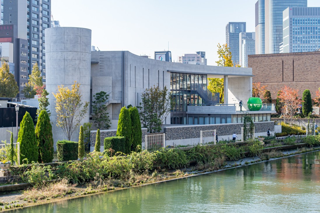 Modern concrete library building with large windows and geometric architecture beside a canal with landscaping