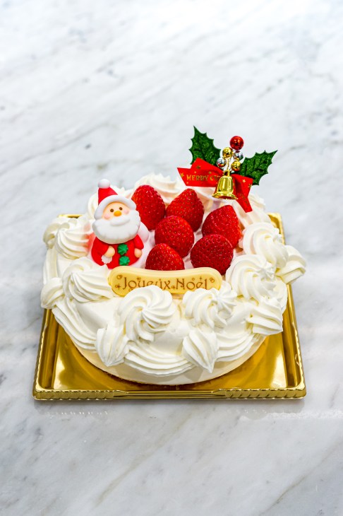 Christmas cake with white frosting, fresh strawberries, Santa decoration and holly garnish on gold plate