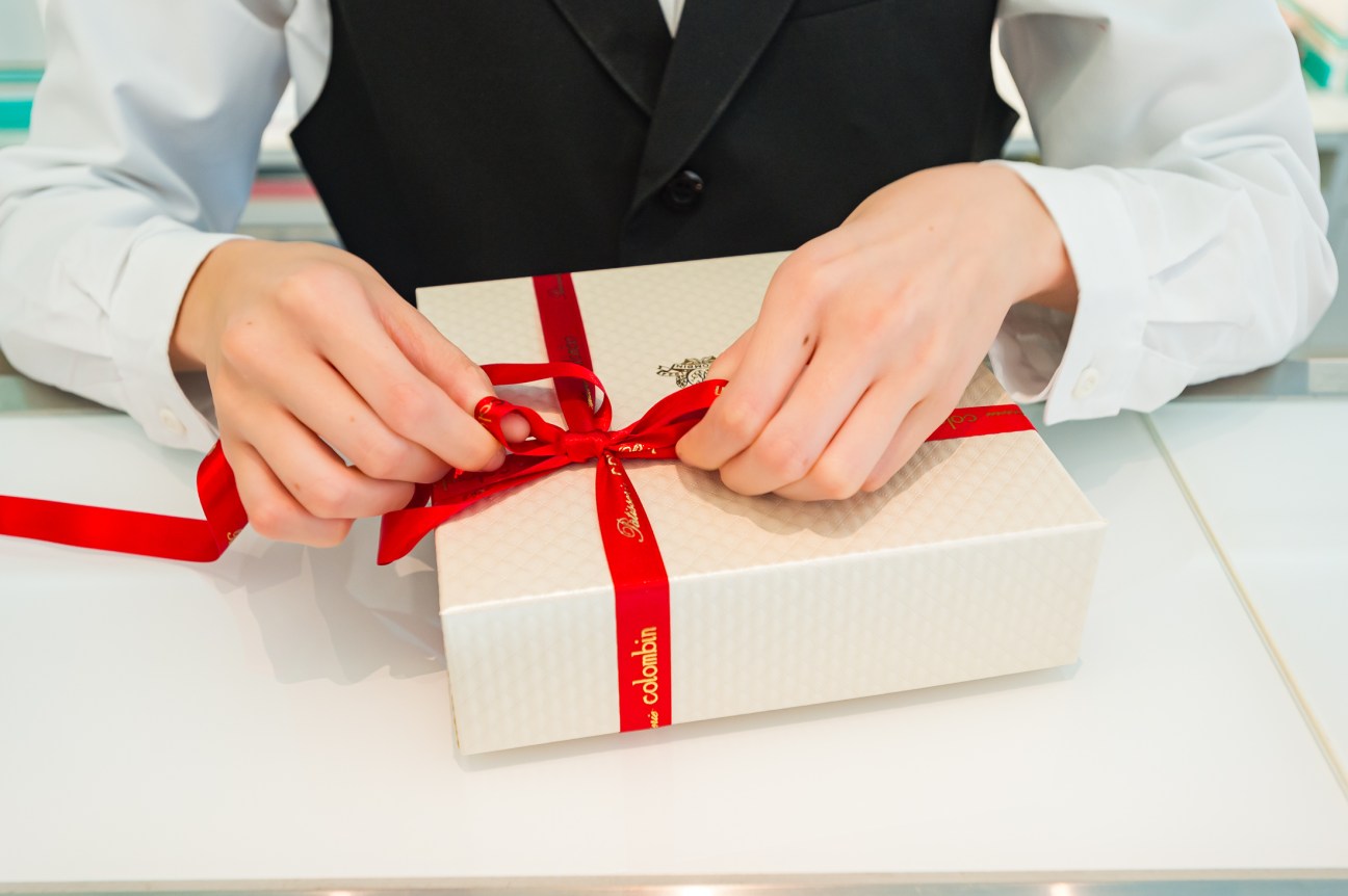 Hands tying red ribbon bow on cream-colored gift box containing traditional German Lebkuchen gingerbread