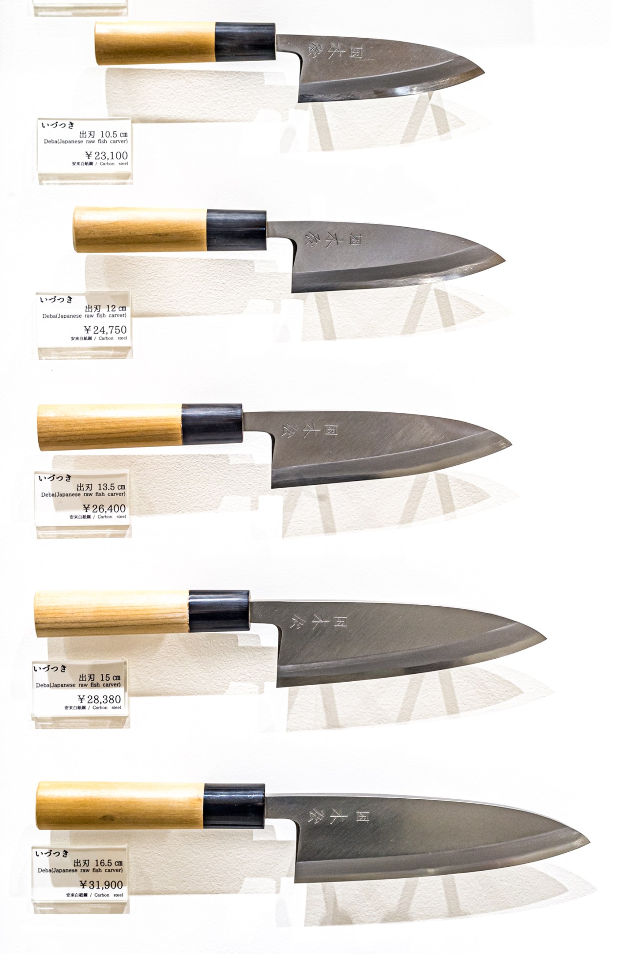 Five Japanese kitchen knives with wooden handles and price tags displayed vertically on white background