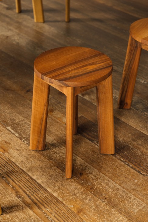 Modern wooden stools with round tops and curved legs on weathered wooden flooring