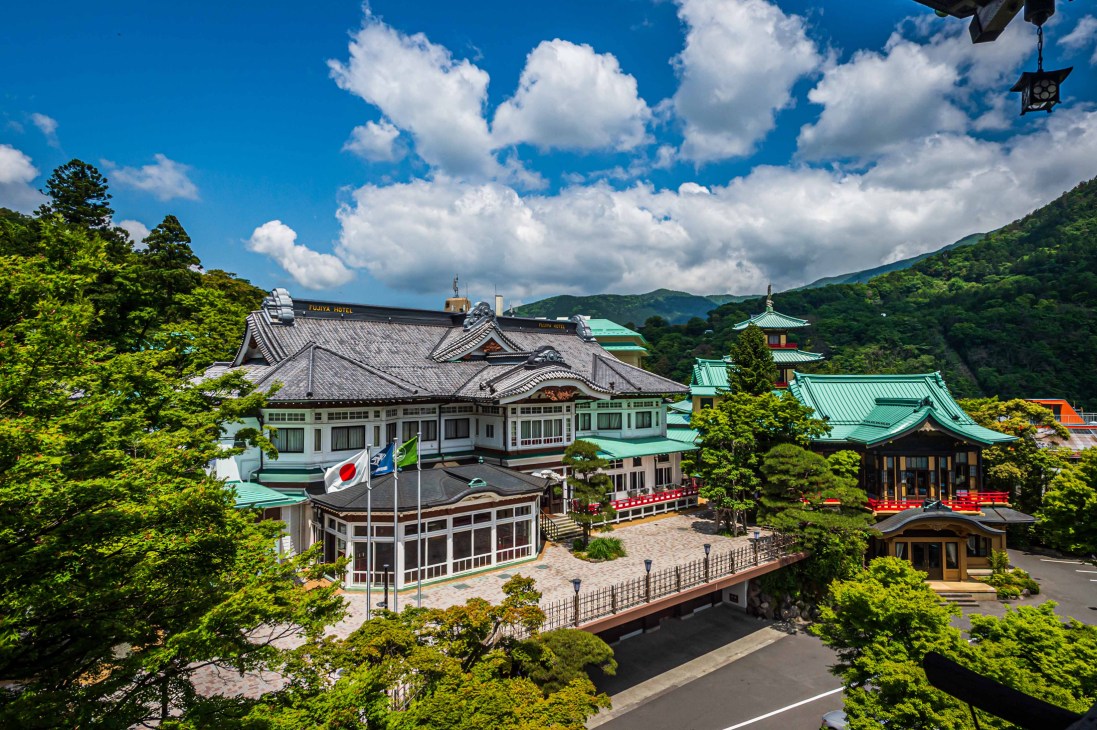 Aerial view of Fujiya Hotel complex nestled in lush green mountains with traditional Japanese architecture and red bridges