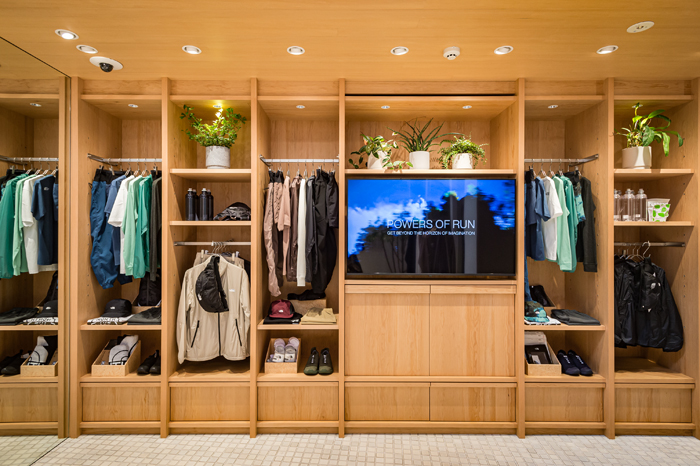 Modern retail interior with wooden built-in shelving displaying clothing, shoes and accessories with integrated TV screen