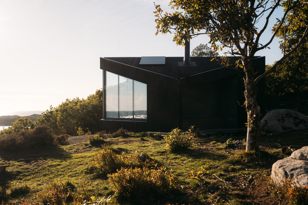 Wooden cabin structure with large glass windows in a forested landscape