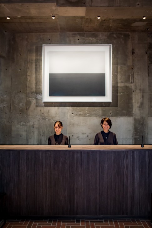 Two women stand at a wooden counter beneath a concrete ceiling and illuminated artwork at Trattoria Babbo.