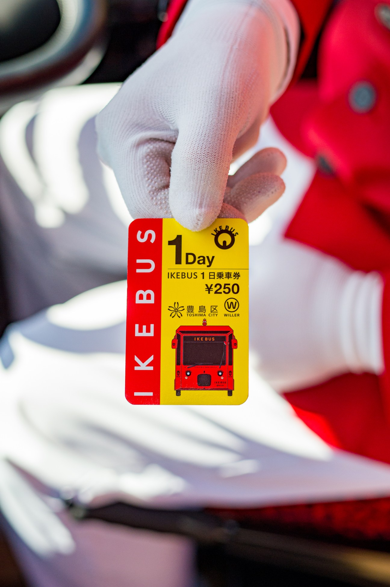 Ikebus day pass ticket held in gloved hand showing red and yellow design with bus illustration and ¥250 price