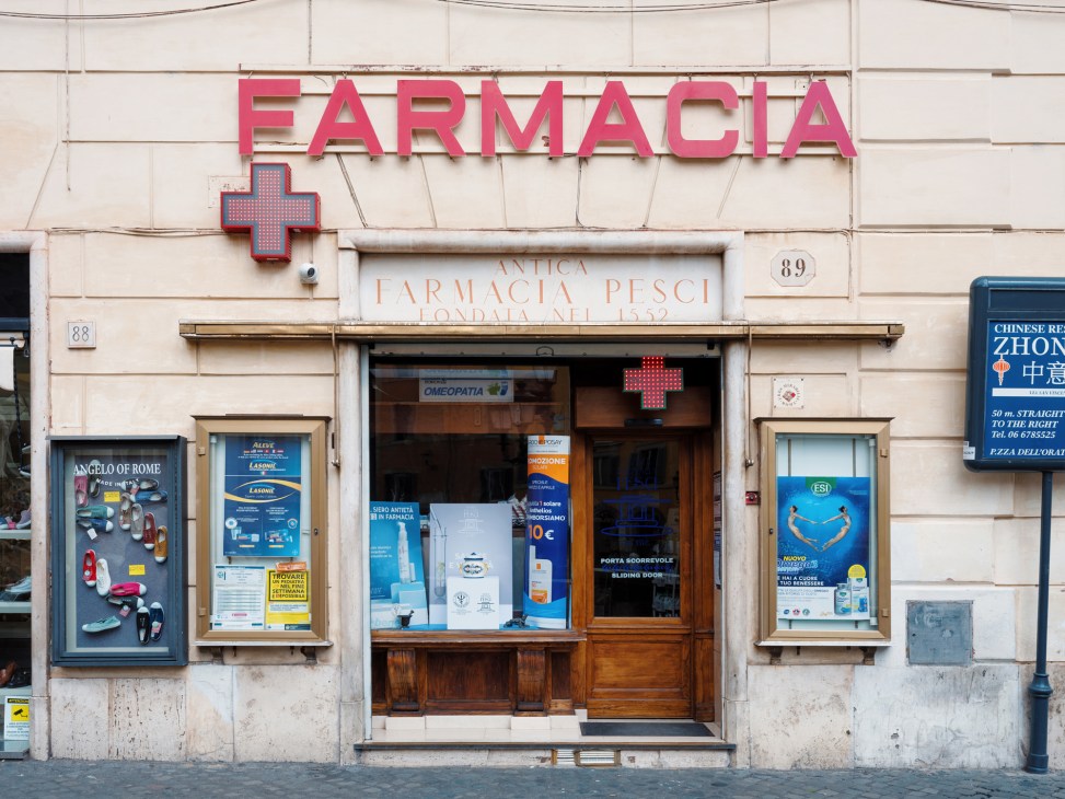 Historic Roman pharmacy storefront with pink neon sign and wooden entrance door.