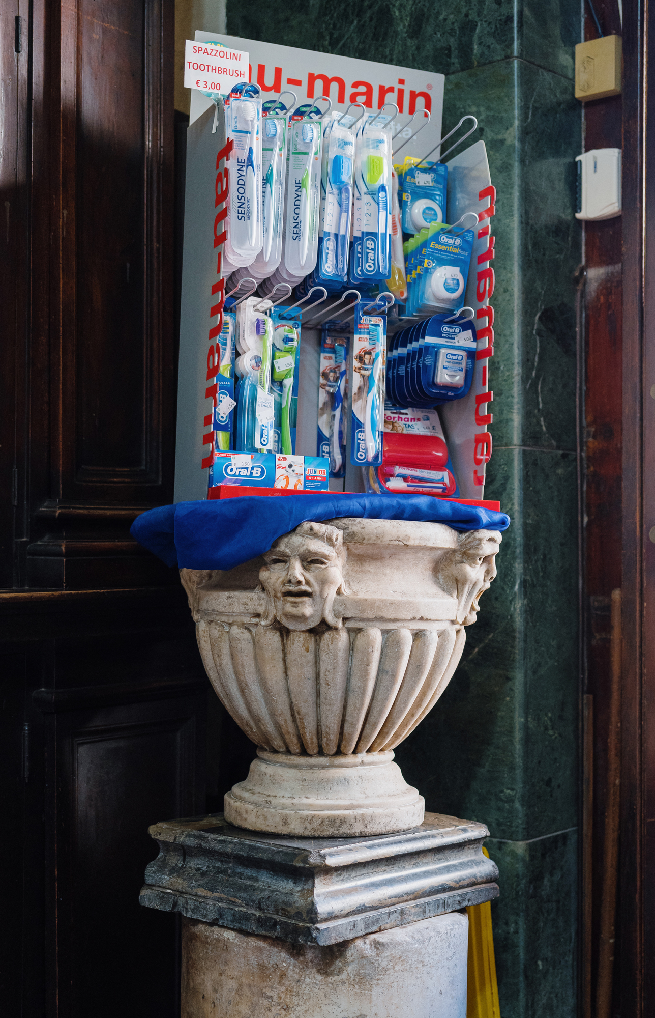 Display of Oral-B toothbrushes and dental products arranged on a decorative white stone urn with blue fabric.