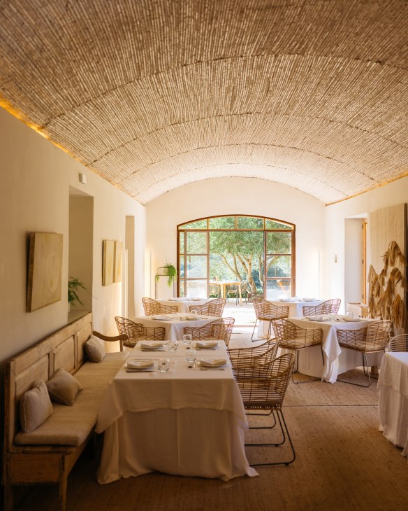Restaurant dining room with exposed brick vaulted ceiling, wicker chairs, white tablecloths and arched window